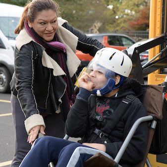 Student in wheelchair getting off bus with teacher
